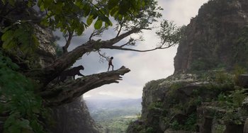 Movie still from “The Jungle Book” (2016), directed by Jon Favreau – A man standing on top of a tree next to a mountain; Extreme Wide shot, Low angle