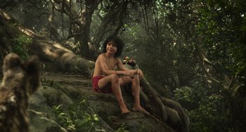 Movie still from “The Jungle Book” (2016), directed by Jon Favreau – A young boy sitting on a rock in the woods; Wide shot, Low angle