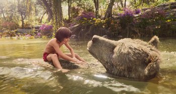 Movie still from “The Jungle Book” (2016), directed by Jon Favreau – A young boy playing with a bear in the water; Wide shot, Overhead angle