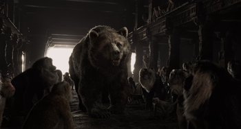Movie still from “The Jungle Book” (2016), directed by Jon Favreau – A group of people gathered around a large bear; Wide shot, Low angle