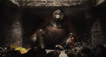 Movie still from “The Jungle Book” (2016), directed by Jon Favreau – A man standing next to a gorilla statue; Wide shot, Low angle