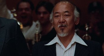 Movie still from “The Karate Kid Part II” (1986), directed by John G. Avildsen – An older man in a white shirt and black jacket; Close Up shot, Low angle