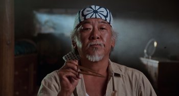 Movie still from “The Karate Kid Part II” (1986), directed by John G. Avildsen – An older man holding a pair of chopsticks in his hand; Close Up shot, Low angle