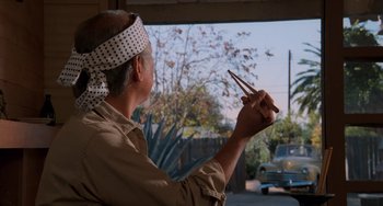 Movie still from “The Karate Kid Part II” (1986), directed by John G. Avildsen – A man holding chopsticks while standing in front of a window; Medium shot, Low angle