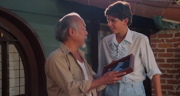 Movie still from “The Karate Kid Part II” (1986), directed by John G. Avildsen – An older man and a young man holding a box; Medium shot, Over the shoulder angle