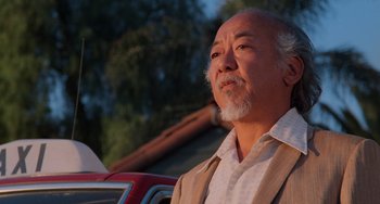 Movie still from “The Karate Kid Part II” (1986), directed by John G. Avildsen – An older man with a goatee is looking at the camera; Close Up shot, Low angle