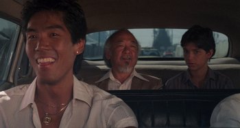 Movie still from “The Karate Kid Part II” (1986), directed by John G. Avildsen – Three men sitting in the back seat of a car; Close Up shot, Over the shoulder angle