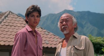 Movie still from “The Karate Kid Part II” (1986), directed by John G. Avildsen – A man standing next to a young man in front of mountains; Medium shot, Low angle