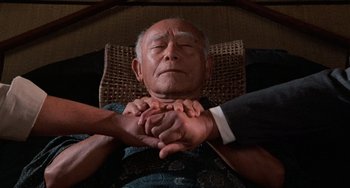 Movie still from “The Karate Kid Part II” (1986), directed by John G. Avildsen – An older man holding hands with a younger man; Medium shot, Overhead angle
