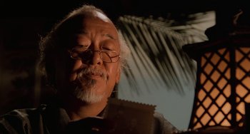 Movie still from “The Karate Kid Part II” (1986), directed by John G. Avildsen – An older man with glasses is looking at a piece of paper; Close Up shot, Over the shoulder angle