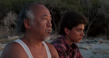 Movie still from “The Karate Kid Part II” (1986), directed by John G. Avildsen – A man sitting next to a young man on a beach; Close Up shot, Low angle