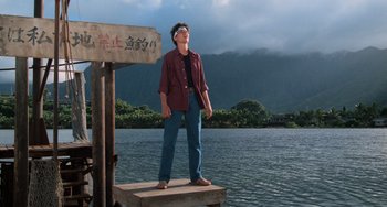 Movie still from “The Karate Kid Part II” (1986), directed by John G. Avildsen – A man standing on a dock near a body of water; Wide shot, Low angle