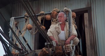 Movie still from “The Karate Kid Part II” (1986), directed by John G. Avildsen – An older man sitting on a boat in the water; Wide shot, Low angle