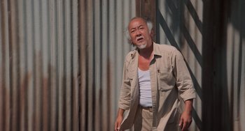 Movie still from “The Karate Kid Part II” (1986), directed by John G. Avildsen – An older man standing in front of a metal wall; Medium shot, Low angle