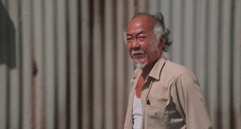 Movie still from “The Karate Kid Part II” (1986), directed by John G. Avildsen – An older man with long hair and a white beard; Medium shot, Low angle