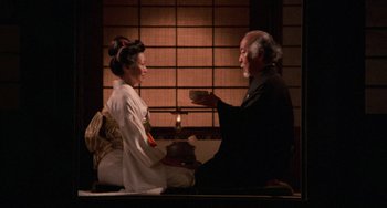 Movie still from “The Karate Kid Part II” (1986), directed by John G. Avildsen – An older man and a young woman sitting on the ground; Medium shot, High angle