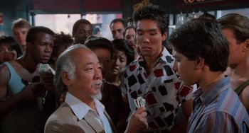 Movie still from “The Karate Kid Part II” (1986), directed by John G. Avildsen – An older man is talking to a group of young men; Medium shot, Over the shoulder angle