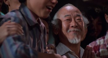 Movie still from “The Karate Kid Part II” (1986), directed by John G. Avildsen – An older man smiling with a young boy next to him; Close Up shot, Low angle