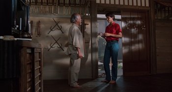 Movie still from “The Karate Kid Part II” (1986), directed by John G. Avildsen – Two men standing next to each other in front of a door; Wide shot, Low angle