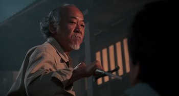 Movie still from “The Karate Kid Part II” (1986), directed by John G. Avildsen – An older man holding a pair of scissors in his hand; Medium shot, Low angle