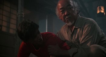 Movie still from “The Karate Kid Part II” (1986), directed by John G. Avildsen – A man and a man in a room with lights on; Medium shot, Low angle