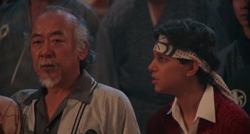 Movie still from “The Karate Kid Part II” (1986), directed by John G. Avildsen – A man standing next to another man wearing a headband; Close Up shot, Low angle