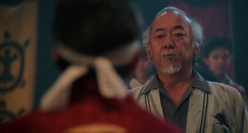 Movie still from “The Karate Kid Part II” (1986), directed by John G. Avildsen – An older man is looking at a woman in red; Close Up shot, Over the shoulder angle