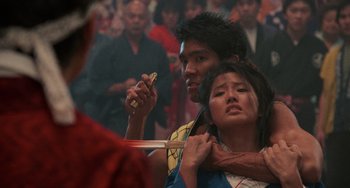 Movie still from “The Karate Kid Part II” (1986), directed by John G. Avildsen – A man and a woman holding a sword in front of a crowd of onlookers; Close Up shot, Over the shoulder angle