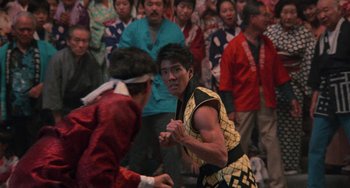 Movie still from “The Karate Kid Part II” (1986), directed by John G. Avildsen – A man in a yellow and black shirt is fighting a man in a red and black shirt; Medium shot, Over the shoulder angle