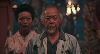 Movie still from “The Karate Kid Part II” (1986), directed by John G. Avildsen – An older man and a younger woman standing together; Close Up shot, Low angle