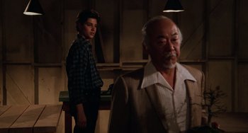 Movie still from “The Karate Kid Part III” (1989), directed by John G. Avildsen – A young man and an older man standing in front of a table; Medium shot, Over the shoulder angle