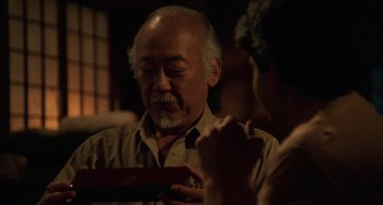 Movie still from “The Karate Kid Part III” (1989), directed by John G. Avildsen – An older man looking down at a box of chocolates; Close Up shot, Over the shoulder angle