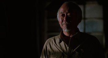 Movie still from “The Karate Kid Part III” (1989), directed by John G. Avildsen – An older man in a brown shirt is looking at the camera; Close Up shot, Low angle