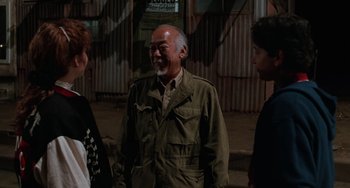 Movie still from “The Karate Kid Part III” (1989), directed by John G. Avildsen – A man in a green jacket standing next to two other people; Medium shot, Over the shoulder angle