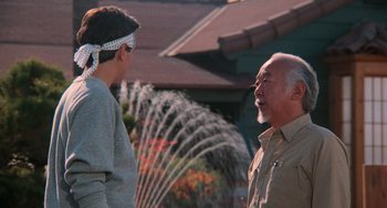 Movie still from “The Karate Kid Part III” (1989), directed by John G. Avildsen – A man and a boy are talking in front of a fountain; Medium shot, Over the shoulder angle