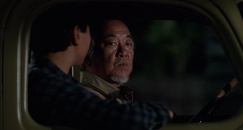 Movie still from “The Karate Kid Part III” (1989), directed by John G. Avildsen – A man sitting in the drivers seat of a car while talking to another man; Close Up shot, Over the shoulder angle
