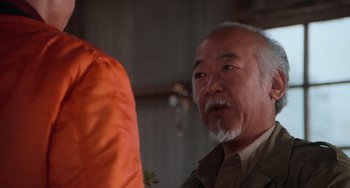 Movie still from “The Karate Kid Part III” (1989), directed by John G. Avildsen – An older man with a beard and mustache wearing an orange jacket; Close Up shot, Over the shoulder angle