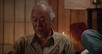 Movie still from “The Karate Kid Part III” (1989), directed by John G. Avildsen – An older man is looking down at his face; Medium shot, Low angle