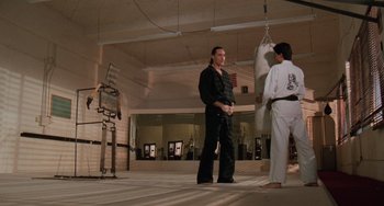 Movie still from “The Karate Kid Part III” (1989), directed by John G. Avildsen – Two men in a gym one is holding a punching bag and the other is standing up; Wide shot, Low angle