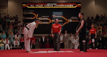 Movie still from “The Karate Kid Part III” (1989), directed by John G. Avildsen – Three men are standing in front of each other on a mat; Wide shot, Low angle