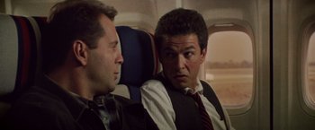 Movie still from “Die Hard” (1988), directed by John McTiernan – Two men sitting next to each other on a plane; Close Up shot, Low angle