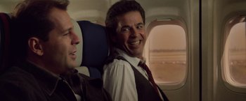 Movie still from “Die Hard” (1988), directed by John McTiernan – A man sitting on a seat in an airplane; Medium shot, Over the shoulder angle