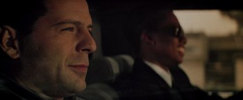 Movie still from “Die Hard” (1988), directed by John McTiernan – A man in a suit sitting next to another man in a suit; Close Up shot, Over the shoulder angle