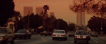 Movie still from “Die Hard” (1988), directed by John McTiernan – Cars driving down a street with palm trees in the background; Extreme Wide shot, Low angle