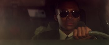 Movie still from “Die Hard” (1988), directed by John McTiernan – A man in a suit and sunglasses sitting in a car; Close Up shot, Low angle