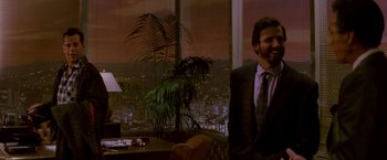 Movie still from “Die Hard” (1988), directed by John McTiernan – A man in a suit and tie standing in front of a window; Medium shot, Over the shoulder angle
