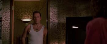 Movie still from “Die Hard” (1988), directed by John McTiernan – A man standing in front of a mirror in a room; Medium shot, Low angle