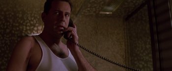 Movie still from “Die Hard” (1988), directed by John McTiernan – A man talking on a phone while wearing a white tank top; Close Up shot, Low angle