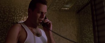 Movie still from “Die Hard” (1988), directed by John McTiernan – A man talking on a phone while wearing a white t - shirt; Close Up shot, Low angle