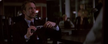 Movie still from “Die Hard” (1988), directed by John McTiernan – A man sitting at a table holding a cell phone; Medium shot, Low angle